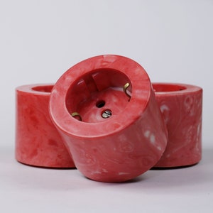 May include: Three red and white marbled electrical outlet covers. The covers are round and have a single electrical outlet in the centre.