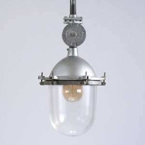 May include: A silver pendant light with a clear glass shade and a metal cage. The light has a vintage industrial style.