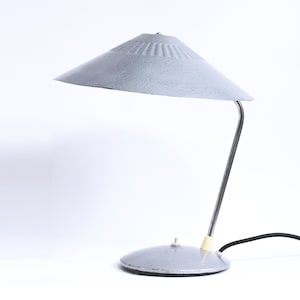 Pode incluir: Uma lâmpada de mesa de metal cinza com um abajur largo e redondo e um braço flexível. A lâmpada tem um design simples e moderno.