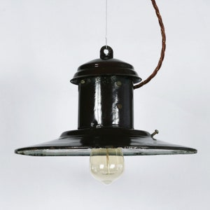 May include: A black metal pendant light with a wide, flat shade and a clear glass light bulb. The light is suspended from a brown cord.