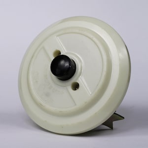 Könnte beinhalten: Ein weißer Lichtschalter aus Keramik mit einem schwarzen Druckknopf. Der Schalter hat eine sternförmige Basis und der Text "CE 230V 50Hz" ist auf der Vorderseite aufgedruckt.