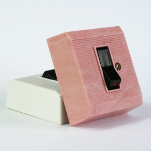 Könnte beinhalten: Ein rosa Lichtschalter aus Kunststoff mit einem schwarzen Kippschalter. Der Schalter ist in der Aus-Position.