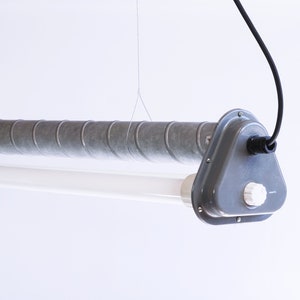 Può includere: Un lampadario a sospensione in metallo grigio di stile industriale con un tubo fluorescente bianco e un cavo nero.