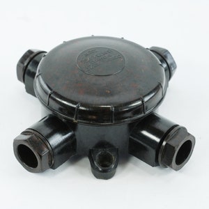 May include: A black bakelite electrical junction box with four ports and a screw-on lid. The lid has the text "MADE IN ENGLAND" printed on it.