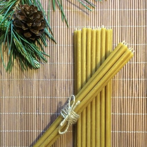 May include: A bundle of 12 natural beeswax candles tied together with twine. The candles are a light yellow color and are arranged on a woven bamboo mat.