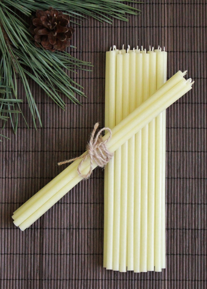 May include: A bundle of 12 thin, pale yellow candles tied together with twine. The candles are arranged on a brown woven mat.