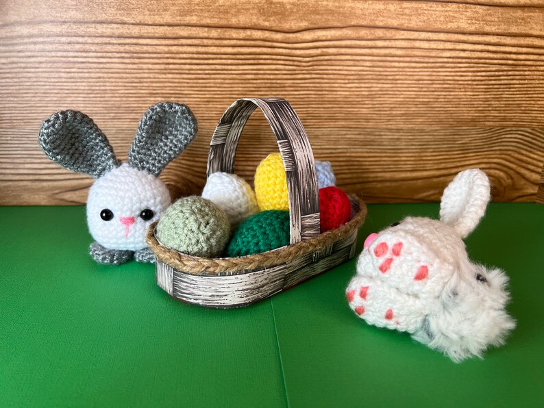 Puede incluir: Dos conejos de crochet, uno sosteniendo una cesta llena de huevos de Pascua de crochet de colores. La cesta est&aacute; hecha de papel tejido y tiene un patr&oacute;n marr&oacute;n y blanco.