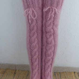 May include: A pair of pink knitted thigh-high socks with a cable knit pattern and a bow at the top of each sock.