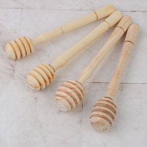 May include: Four wooden honey dippers with a natural finish. The dippers have a long handle and a rounded, grooved end for scooping honey.