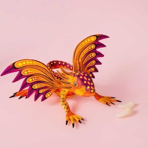 May include: A hand-painted wooden figurine of a mythical creature with a lizard-like body, large orange and yellow wings with purple accents, and intricate dot patterns in shades of yellow, orange, and purple covering its entire surface.