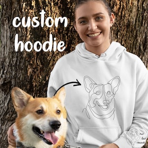 May include: White hoodie with a black line drawing of a corgi on the front. The text "custom hoodie" is in black text at the top of the image. A corgi is sitting next to the person wearing the hoodie.