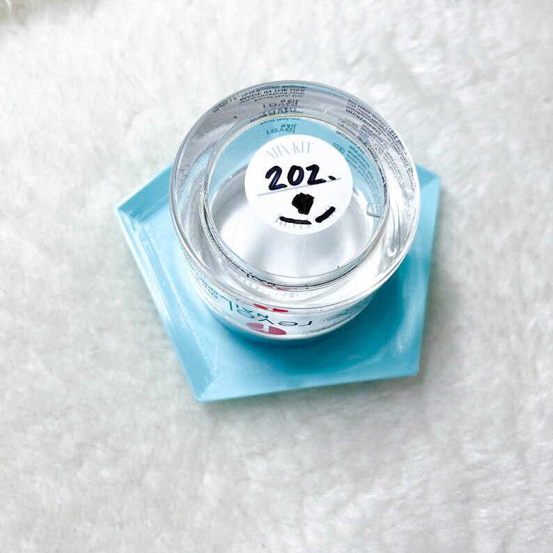 May include: A clear glass measuring cup with a white sticker that says "Mix It 20z." The cup is sitting on a light blue hexagonal tray.