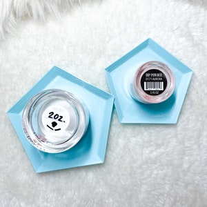 May include: Two containers of nail dip powder on blue hexagonal trays. One container is clear with a white label that says "2 oz." The other container is pink with a black label that says "Dip Powder D171 Aurora 5 FL OZ."