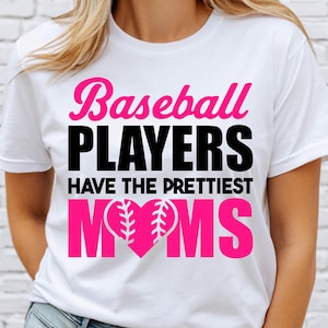 Op de afbeelding: Wit T-shirt met de tekst "Baseball PLAYERS HAVE THE PRETTIEST MOMS" in roze en zwart. Het woord "MOMS" heeft een hartvormig ontwerp met honkbalstiksels.