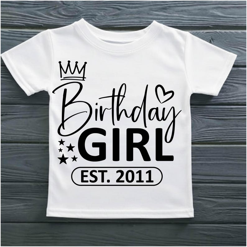 May include: White t-shirt with the text "Birthday GIRL EST. 2011" in black script and block letters. The design includes a crown, stars, and a heart. A cute tee for a birthday celebration.