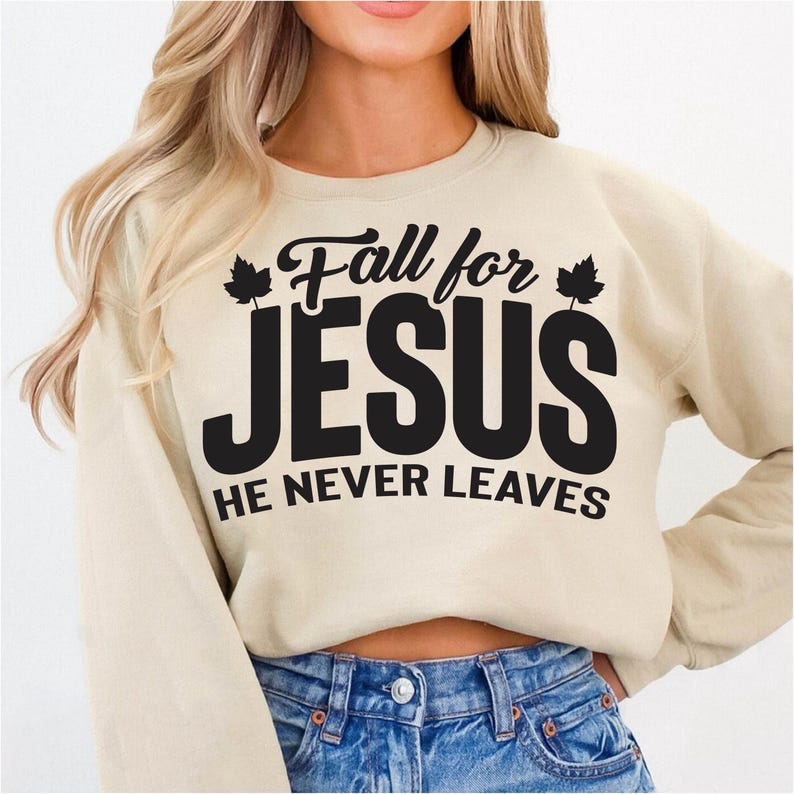 May include: Beige sweatshirt with the text "Fall for JESUS HE NEVER LEAVES" in black. The text is centered on the front of the sweatshirt. The sweatshirt has long sleeves and a crew neck.