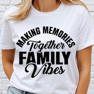 May include: White crew neck t-shirt featuring the black text "MAKING MEMORIES Together FAMILY Vibes". The text is in a mix of fonts, with the word "Together" in a cursive style. The shirt is made of a soft material.