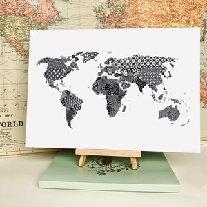 May include: A black and white world map print with a patterned design. The map is printed on white paper and is displayed on a wooden easel.