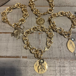 May include: Four gold chain bracelets with religious medallions and crystal accents. Each bracelet features a different medallion, including a cross, a heart, and two oval medallions.