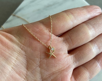May include: A gold chain necklace with a small starfish pendant and a clear gemstone. The pendant is attached to the chain with a small loop.