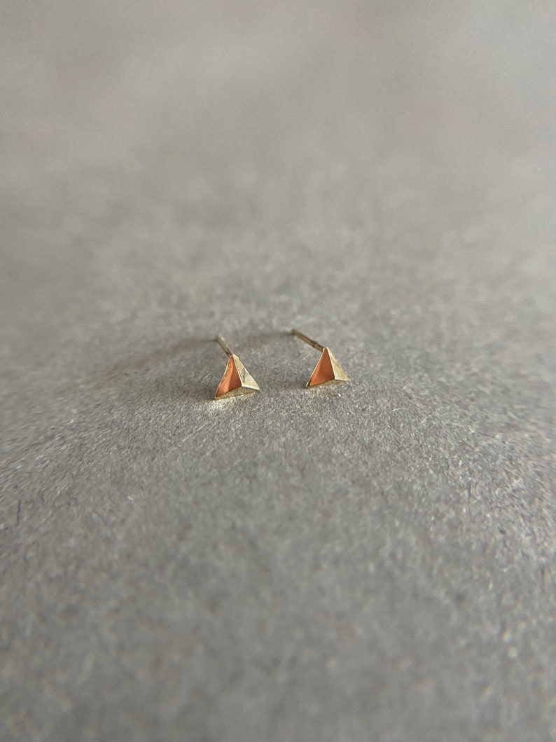 K&ouml;nnte beinhalten: Ein Paar goldene Dreiecks-Ohrstecker. Die Ohrringe sind klein und zart.