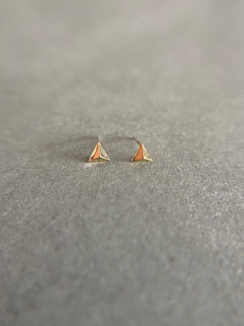 K&ouml;nnte beinhalten: Ein Paar goldene Dreiecks-Ohrstecker. Die Ohrringe sind klein und zart und haben ein schlichtes, modernes Design.
