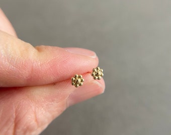 Könnte beinhalten: Ein Paar goldene Ohrstecker mit einem kleinen, strukturierten Blumenmuster.