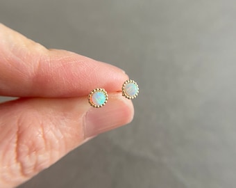 May include: A pair of gold earrings with small white opal stones set in a beaded bezel.