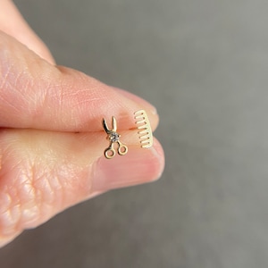 May include: A pair of gold earrings featuring a small pair of scissors with a single diamond and a small comb.