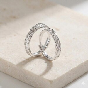 Peut inclure: Deux bagues en argent avec un motif complexe en forme de vagues. Les bagues sont posées sur une surface de couleur claire. Les bagues sont probablement réglables et sont un bijou romantique.