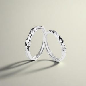 Op de afbeelding: Twee zilveren ringen met zwart-witte decoratieve details. Eén ring heeft een bamboe-achtig ontwerp, de andere heeft bloemen- en geometrische patronen. De ringen worden getoond tegen een neutrale achtergrond.