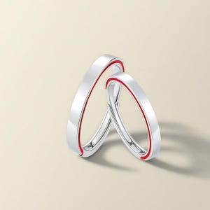 Puede incluir: Dos anillos plateados con una banda interior roja. Los anillos tienen un acabado liso y brillante y un diseño moderno y minimalista. Los anillos son probablemente para una pareja, simbolizando el compromiso y el amor.