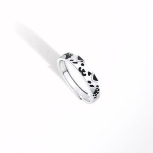 May include: A silver-toned ring featuring a repeating pattern of black enamel paw prints and small heart shapes around the outer band. The ring has an open-ended design, allowing for adjustment, and displays a polished metallic finish throughout.