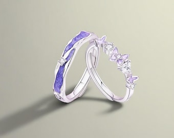 May include: Two silver rings. One ring features a purple enamel design with a small diamond. The other ring has a row of small purple butterfly designs and diamonds. The rings are set against a neutral background.