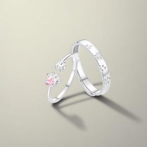 Op de afbeelding: Twee zilveren ringen. Eén ring heeft een roze pootvormige edelsteen. De andere ring heeft pootafdruk graveringen. De ringen worden gepresenteerd op een lichtgrijze achtergrond.
