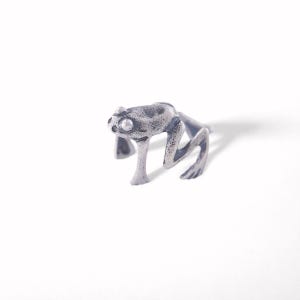 May include: A silver-colored frog figurine with a textured surface. The frog is in a crouching position, with its legs bent and its eyes visible. The figurine is set against a white background.