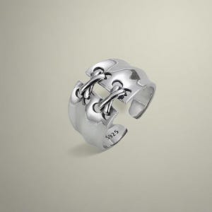 May include: A silver ring with a unique design featuring a criss-cross pattern. The ring is marked with the number "S925", indicating it is made of sterling silver.