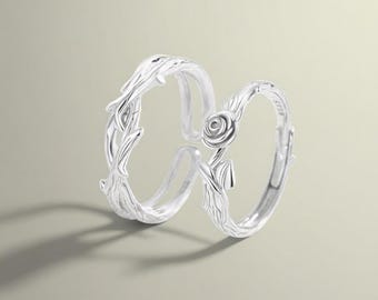 May include: A pair of silver rings with a rose design. The rings are intertwined and feature a delicate floral pattern.