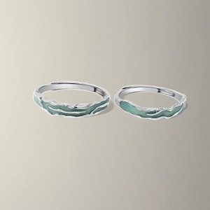 Könnte beinhalten: Zwei silberne Ringe mit einem hellgrünen Emaille-Design. Die Ringe sind schlicht und elegant und wären ein tolles Geschenk für ein Paar.