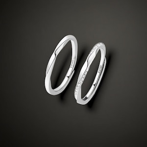 Op de afbeelding: Twee zilveren ringen, een met een gedraaid ontwerp en de andere met een rij kleine, heldere stenen.