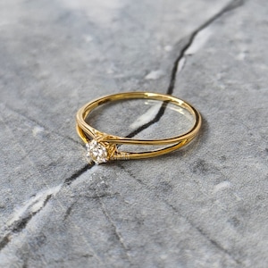 May include: A delicate gold ring with a single, round diamond set in the center. The band is thin and features a simple, elegant design.