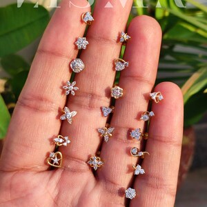 May include: A collection of 17 gold nose rings with various designs, including hearts, stars, flowers, and butterflies. Each ring is adorned with sparkling diamonds.