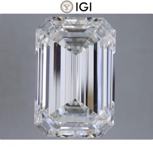 May include: A large, clear emerald-cut diamond with a rectangular shape and faceted surfaces. The diamond is set against a neutral gray background, showcasing its brilliance and clarity. The IGI logo is in the top left corner.