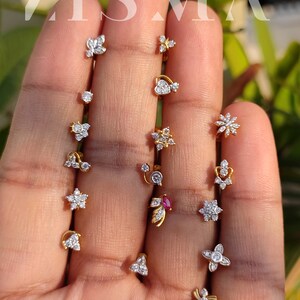 May include: A collection of 14 gold nose rings with various designs featuring small diamonds. The designs include a heart, a flower, a star, a leaf, and a swirl.