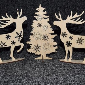 May include: Three wooden Christmas decorations: a Christmas tree and two reindeer. The tree and reindeer are decorated with black snowflakes.