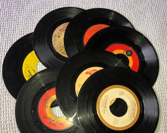 Puede incluir: Una pila de siete discos de vinilo negros con etiquetas de colores. Las etiquetas muestran títulos de canciones, nombres de artistas y sellos discográficos como "MCA Records" y "Capitol Records".
