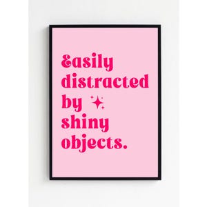 Puede incluir: Fondo rosa con marco negro y texto blanco que dice "Fácilmente distraído por objetos brillantes."