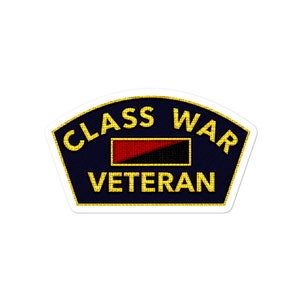 May include: A blue and gold sticker with the text "Class War Veteran" and a red and black flag.