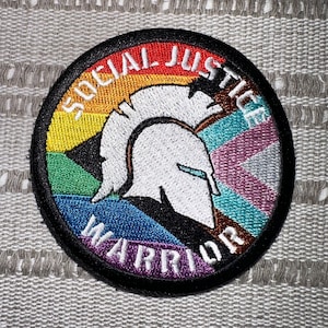 May include: A black and white embroidered patch with a rainbow background. The patch features a stylized Spartan helmet and the text "Social Justice Warrior".