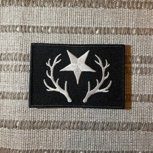 Può includere: Toppa ricamata nera con una stella bianca a cinque punte e due corna bianche.